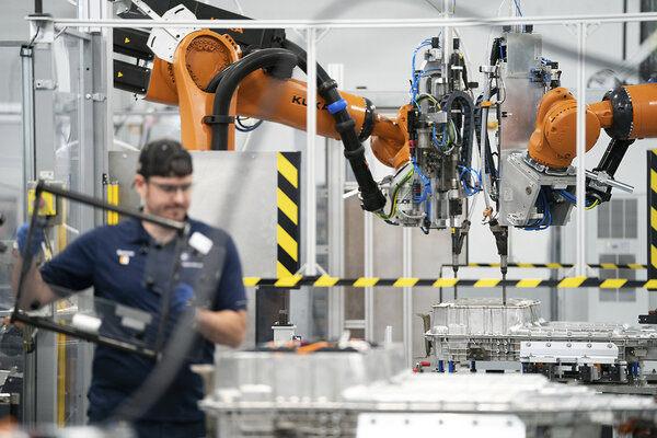 An employee in a blue uniform and a robot, side by side, complete tasks in the battery assembly hall at a BMW plant.